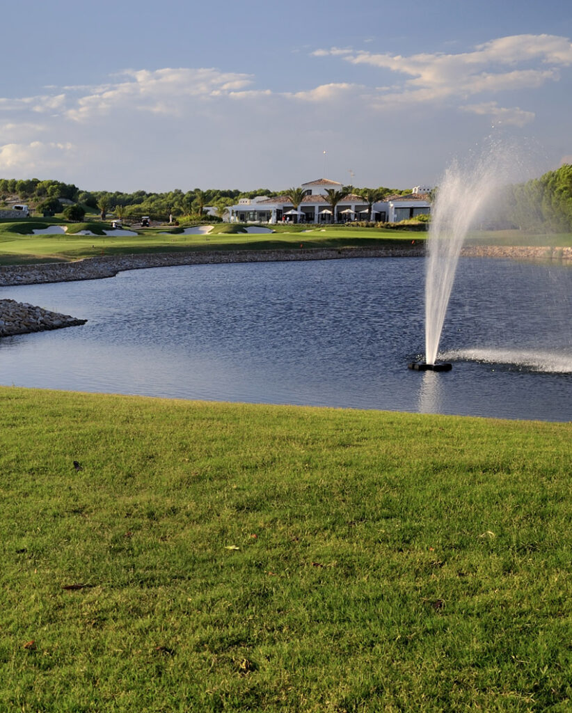 Vista del campo de golf de Las Colinas con un lago, una fuente en primer plano y la casa club al fondo
